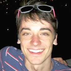 A smiling man with short brown hair wearing a blue striped shirt and sunglasses on his head.